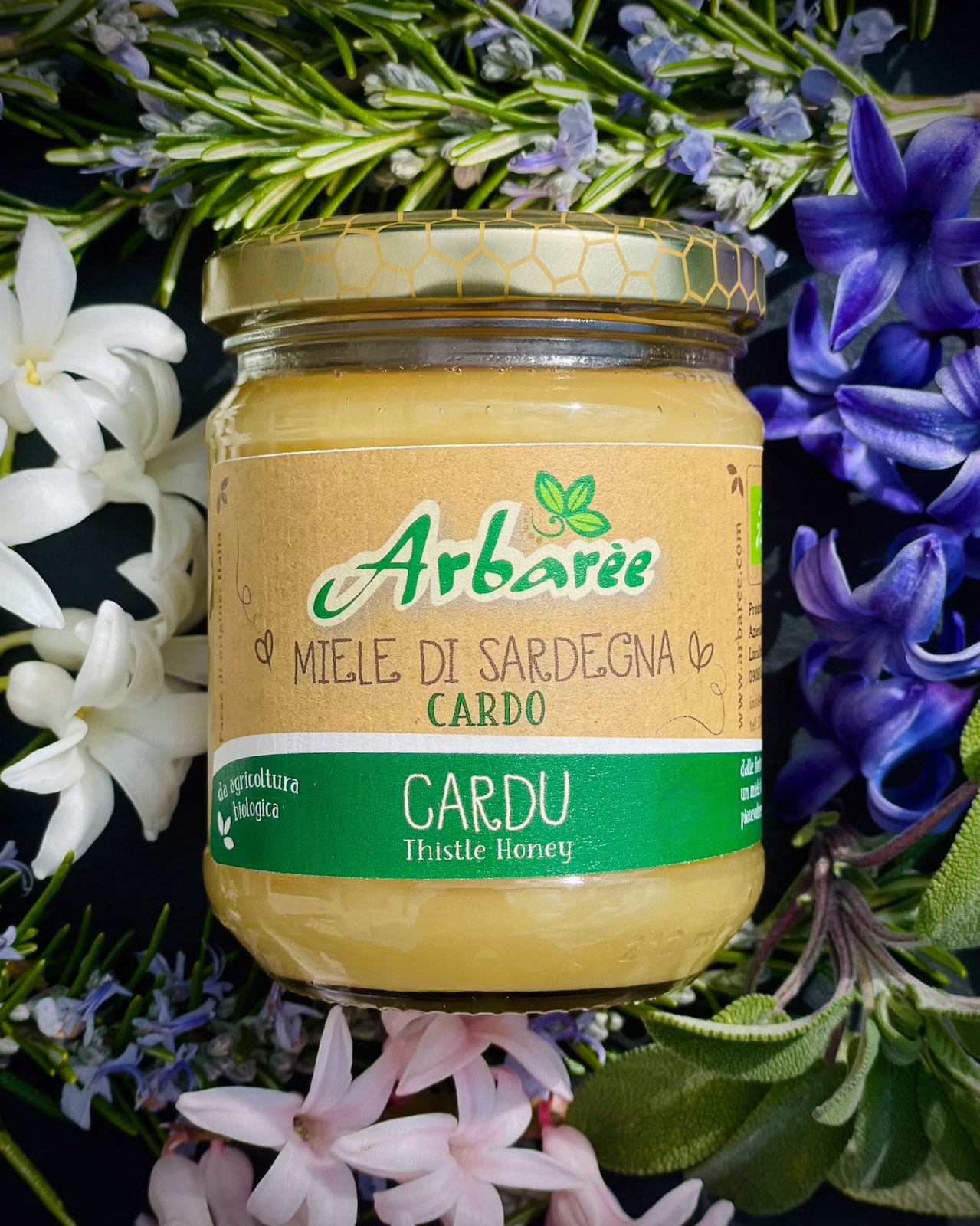 Jar of Arbaree Cardu honey surrounded by flowers and herbs