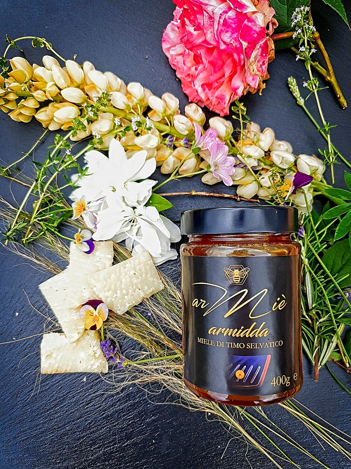 Jar of Sardinian wild thyme honey with a decorative arrangement of flowers on a dark surface