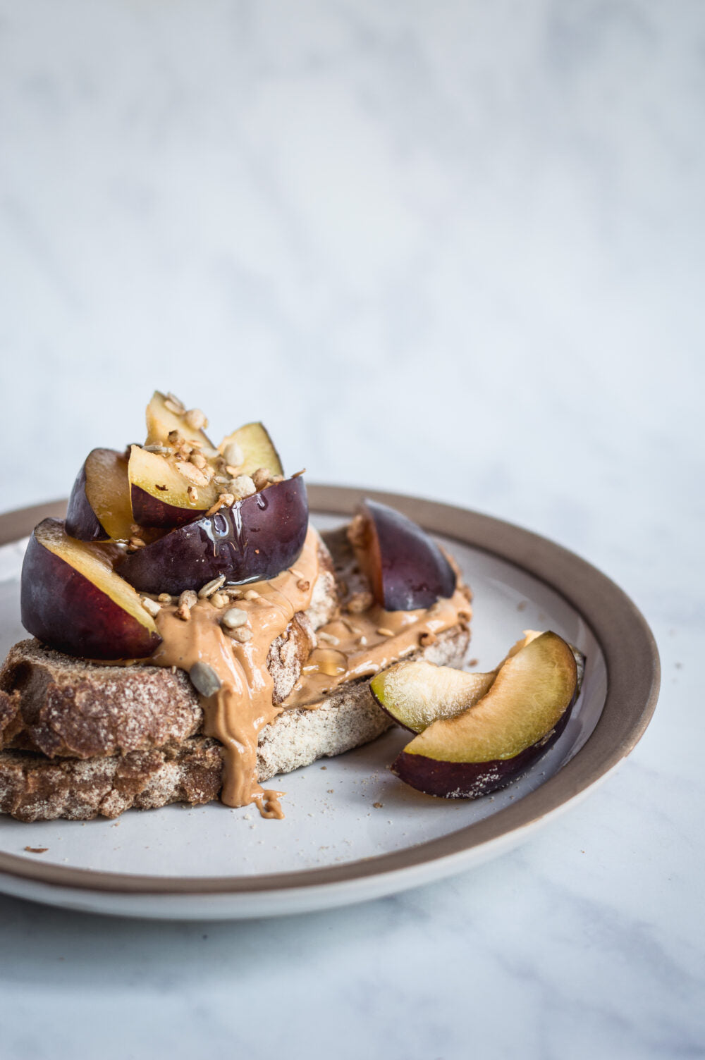 Plated dish with toast, plums, and peanut butter on a light background
