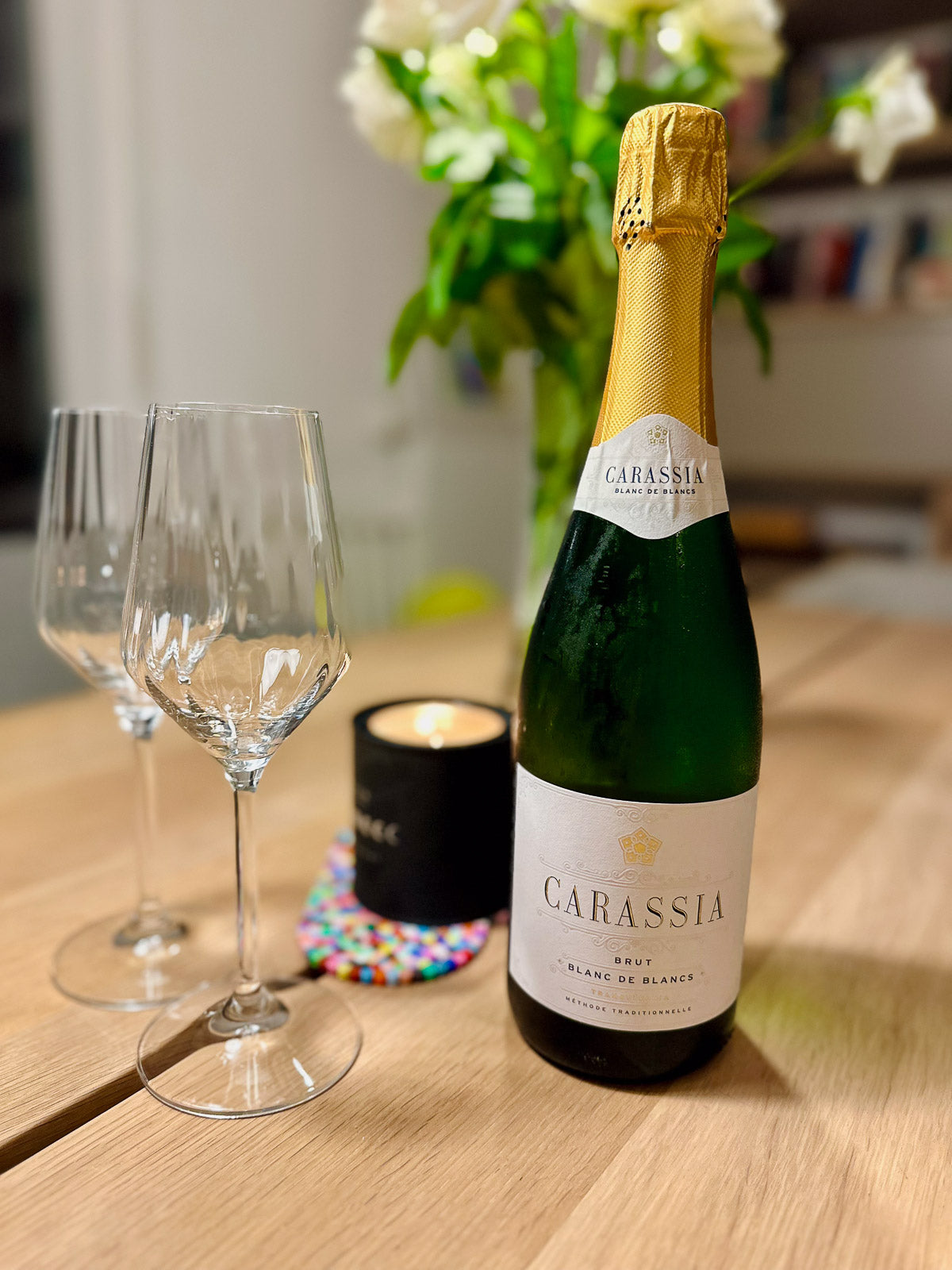 Bottle of Carassia blanc de blancs sparkling winee with two glasses on a wooden table.