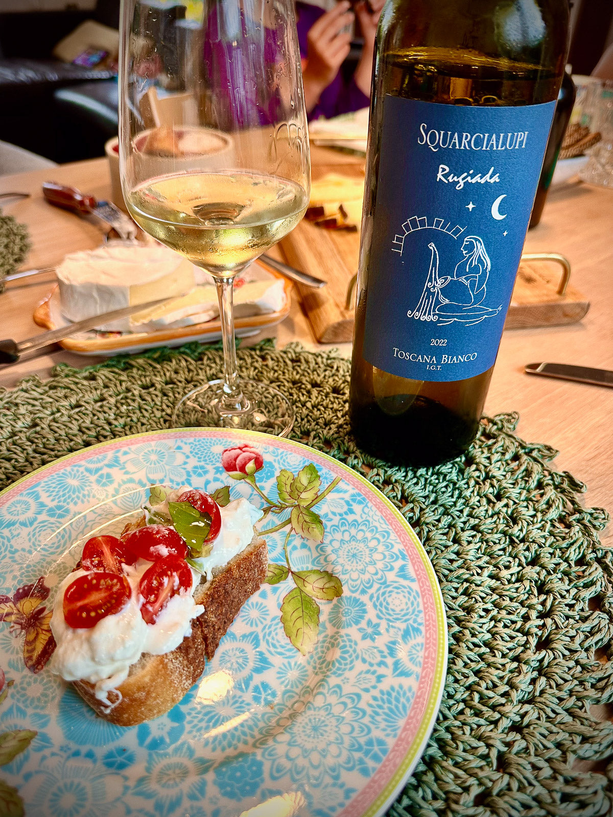 Wine bottle labeled 'Squarcialupi' with a glass of wine and a plate of food on a table.