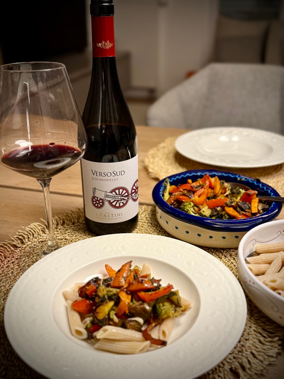 Dinner setting with pasta dish, a bottle of Susumaniello wine called Versosud, and glass on a table.