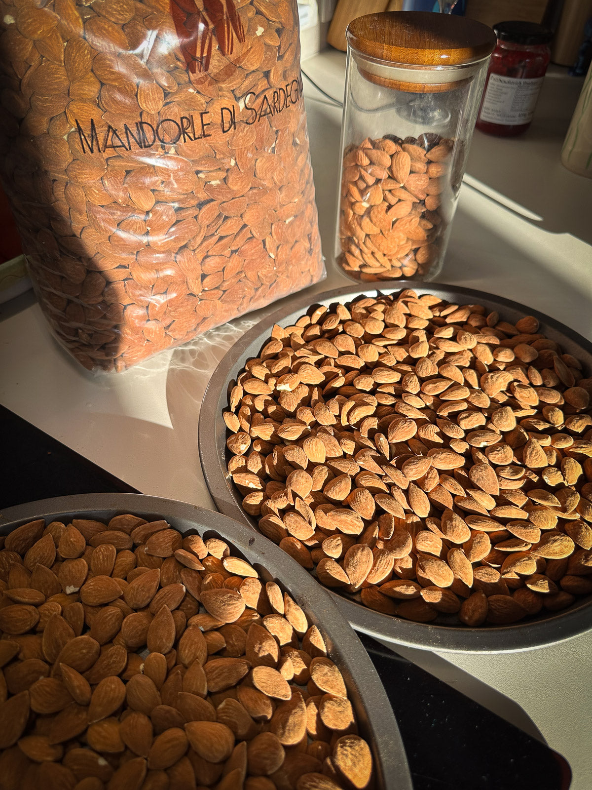 Almonds in a bowl with a jar labeled 'Mandorle di Sardegna' on a kitchen counter.