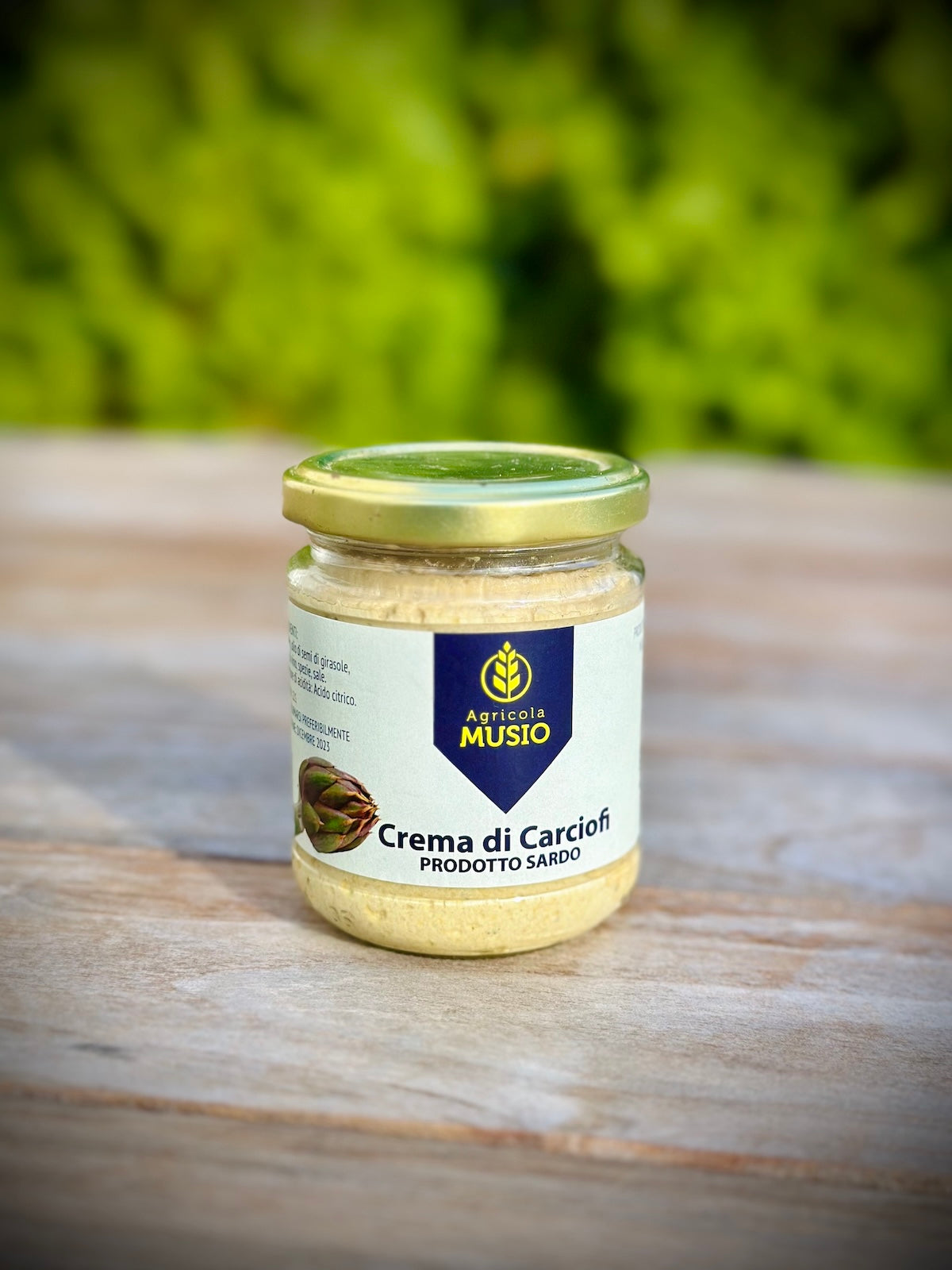 Jar of 'Crema di Carciofi' on a wooden surface with a blurred green background