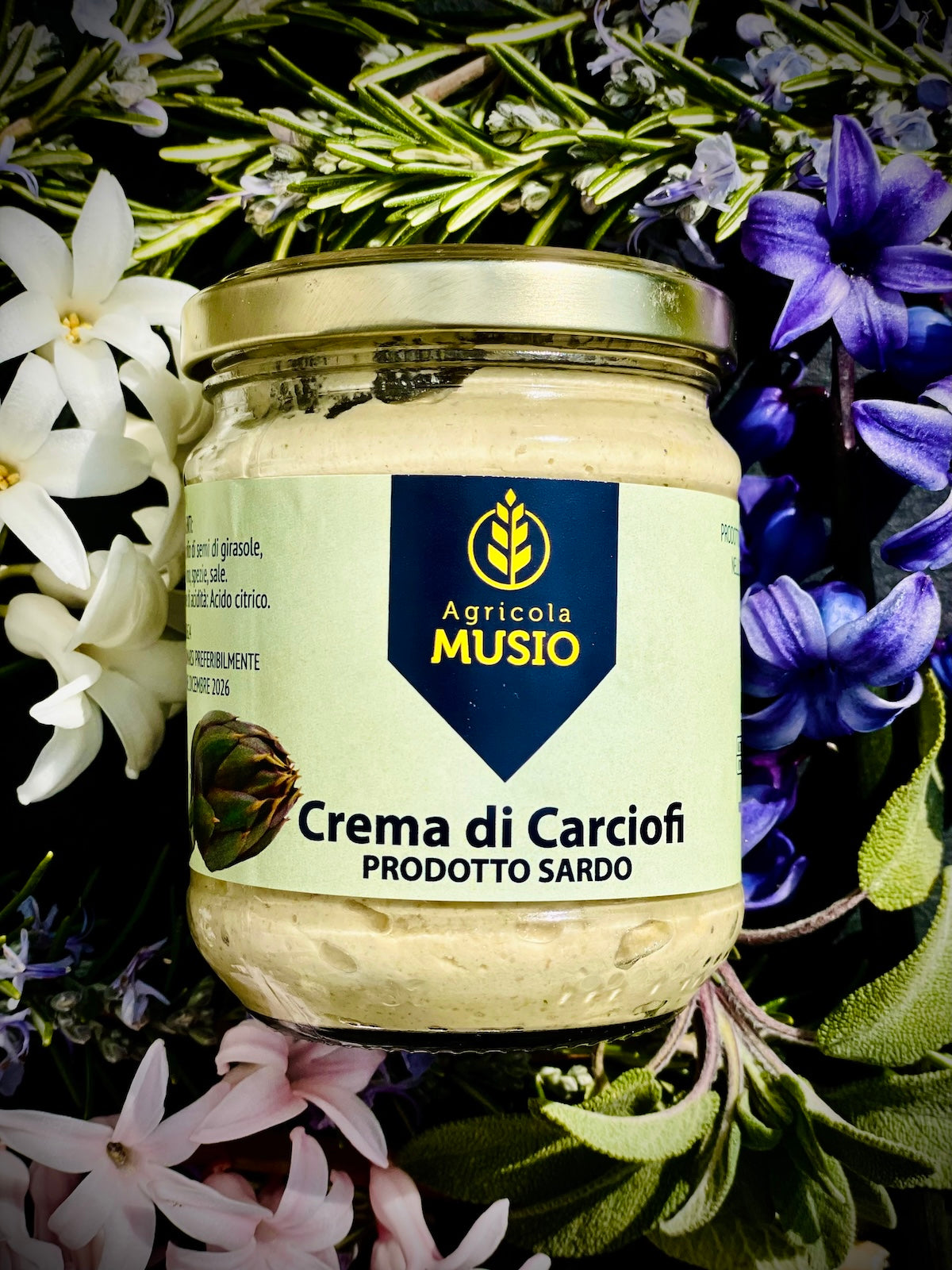 Jar of 'Crema di Carciofi' surrounded by flowers and herbs with 'Agricola Musio' label.
