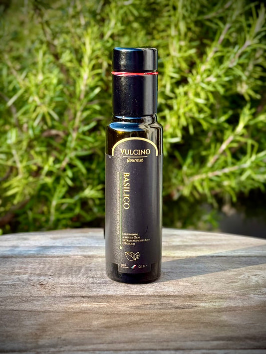 Black bottle of Vulcino basilico oil on a wooden surface with greenery in the background