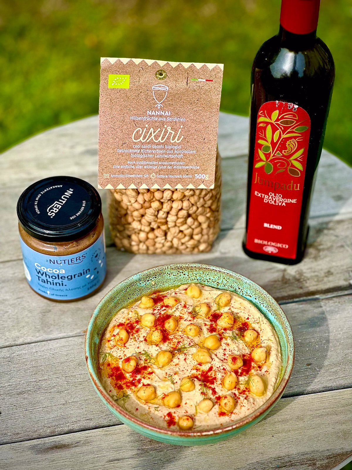 Bowl of hummus with chickpeas, a bottle of wine, and a jar on a wooden surface.
