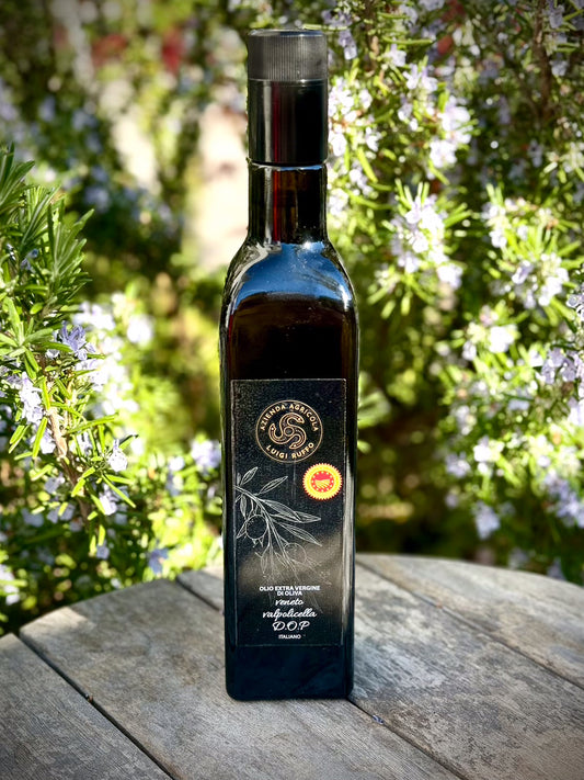 Bottle of olive oil with a label on a wooden surface with greenery in the background