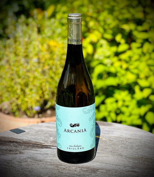 Bottle of Arcania wine on a wooden surface with a blurred green background