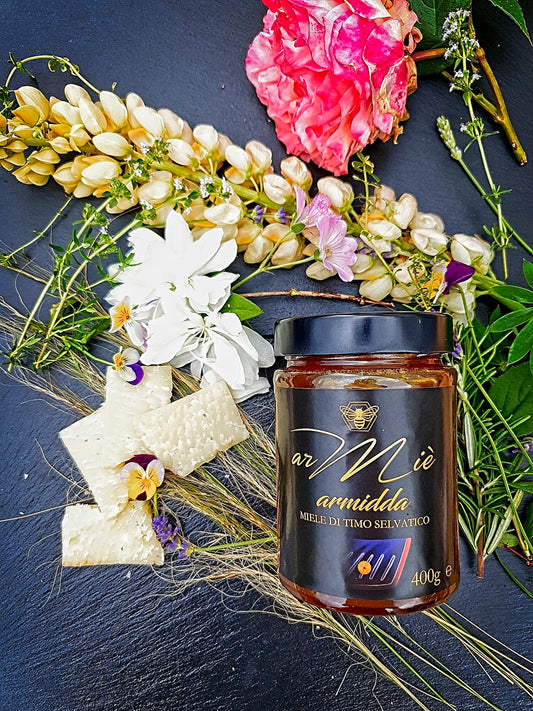 Jar of Sardinian wild thyme honey with a decorative arrangement of flowers on a dark surface