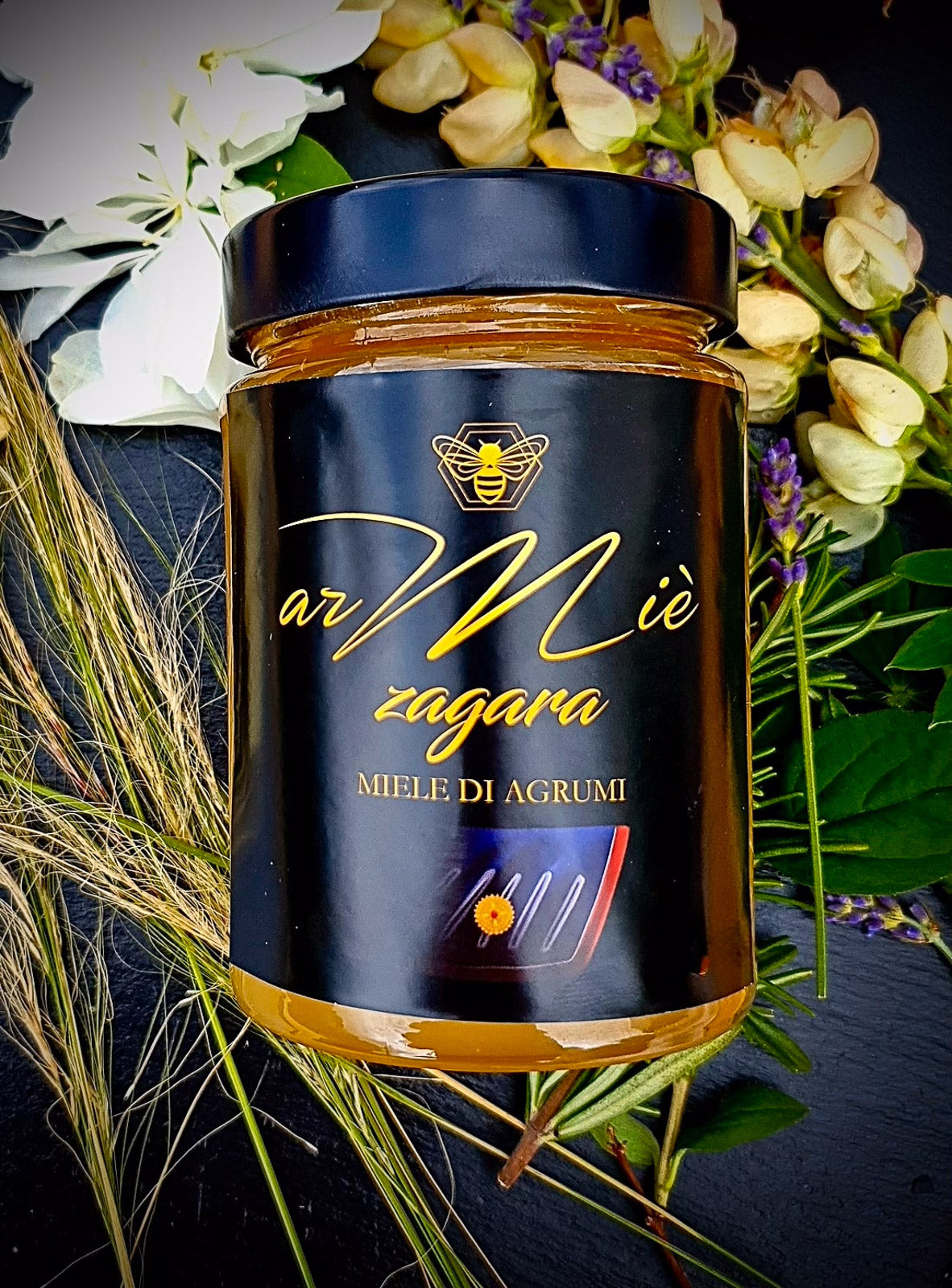 Glas Zitrusfruchthonig mit Blumen- und Grünarrangement auf dunkler Oberfläche