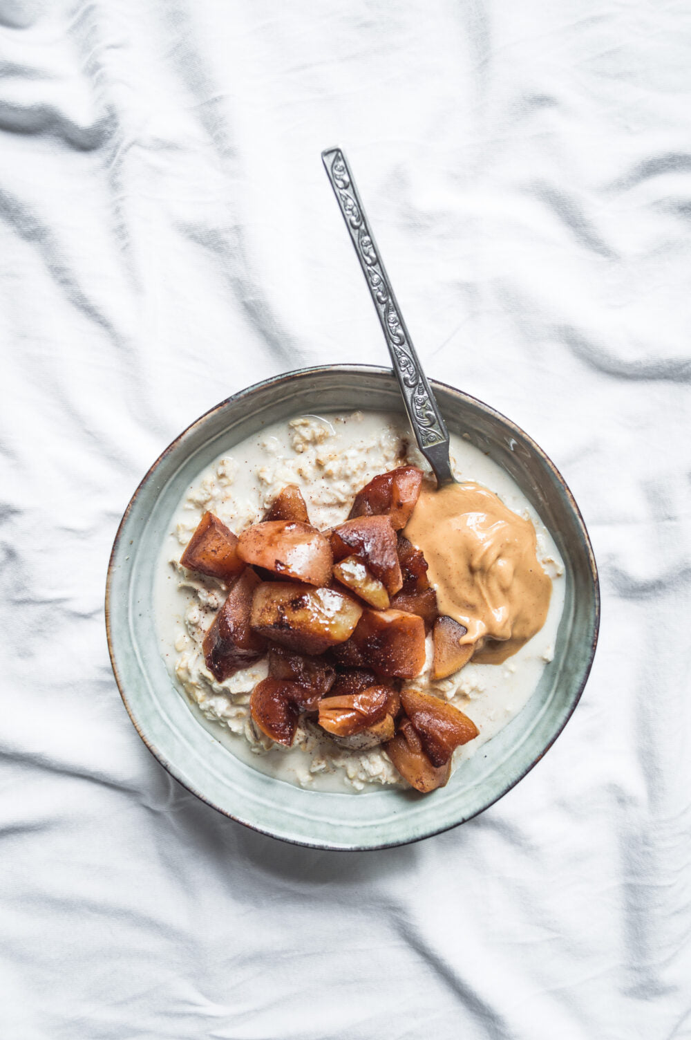 Bowl of oatmeal with apples and peanut butter on a light gray background