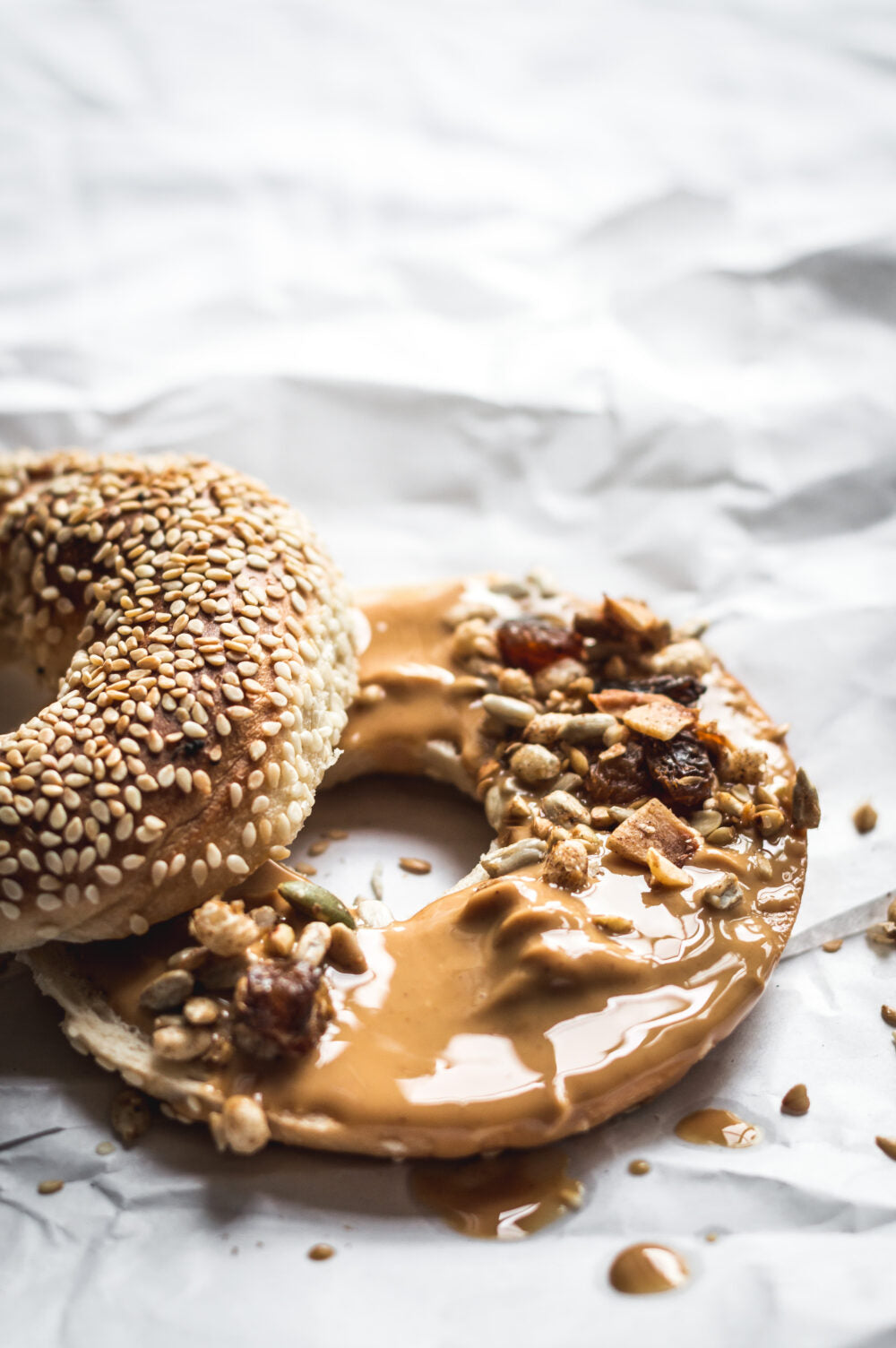 Bagel with sesame seeds and another with peanut butter and raisins on a white marble surface.
