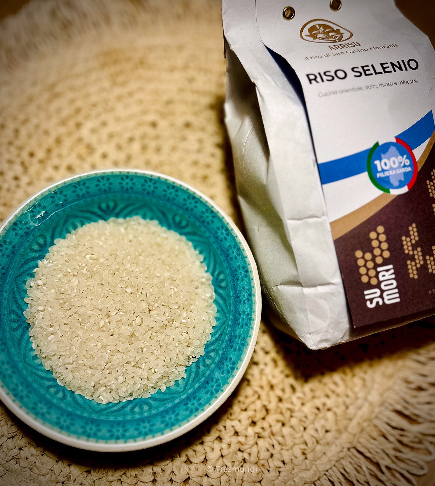 Rice in a blue bowl next to a bag of Su Mori Riso Selenio on a textured surface