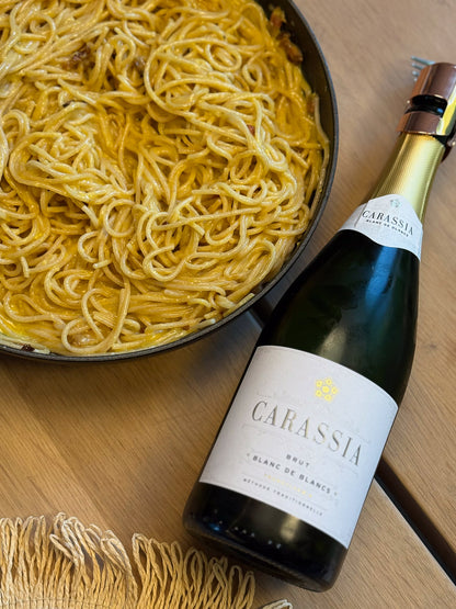 Bottle of Carassia blanc de blancs sparkling wine next to a pan of spaghetti on a wooden table