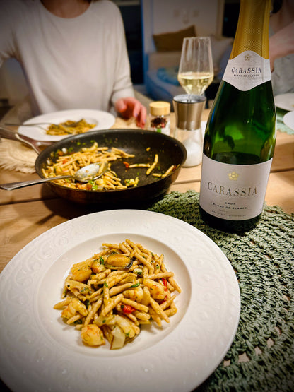 Pasta dish on a plate with a bottle of Carassia blanc de blancs sparkling wine and a glass in the background.