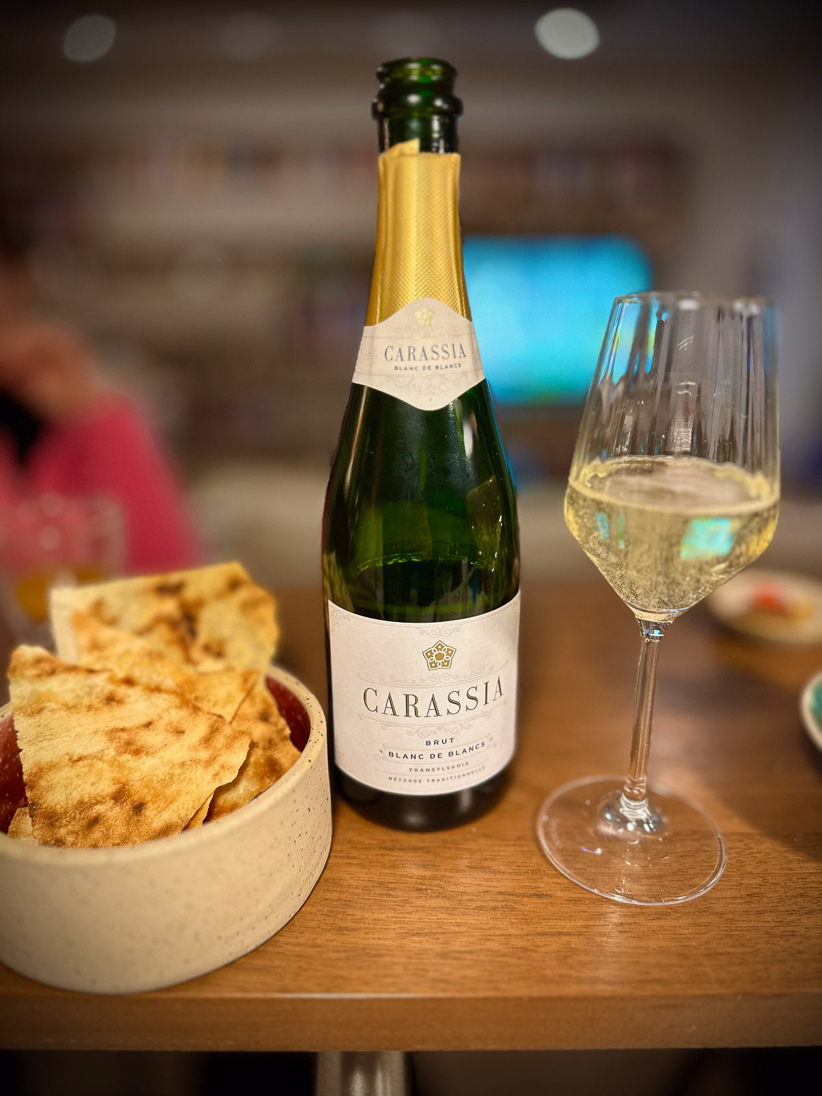 Bottle of Carassia blanc de blancs sparkling wine with a glass of wine and snacks on a table.