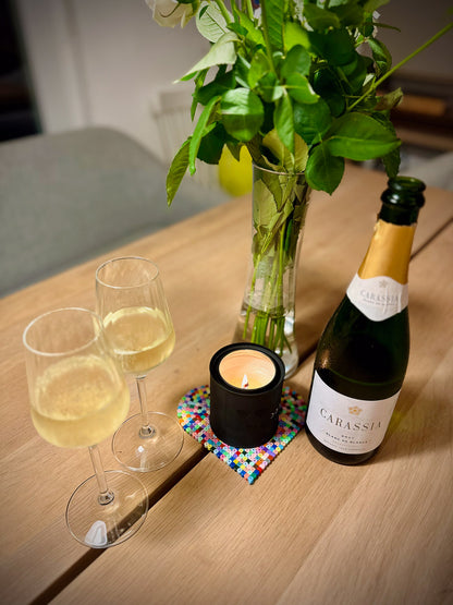 Two glasses of white wine, a bottle of Carassia blanc de blancs sparkling wine, a candle, and a vase with flowers on a wooden table.