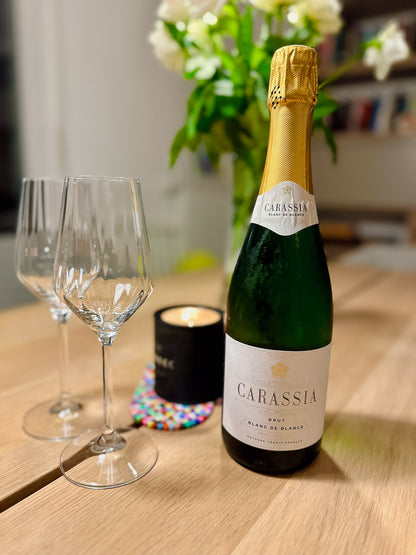 Bottle of Carassia blanc de blancs sparkling winee with two glasses on a wooden table.