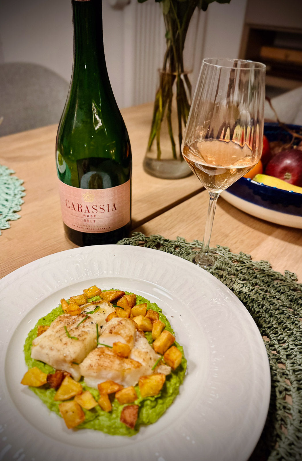 Dinner setting with a dish of fish and vegetables, a bottle of Carassia sparkling wine, and a glass of white wine.
