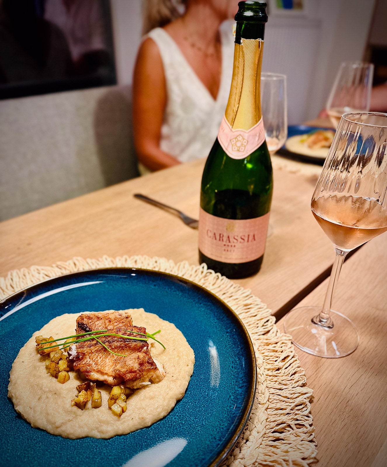 Dinner table with a plate of food, a bottle of Carassia wine, and a glass of wine.