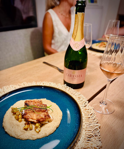 Dinner table with a plate of food, a bottle of Carassia wine, and a glass of wine.