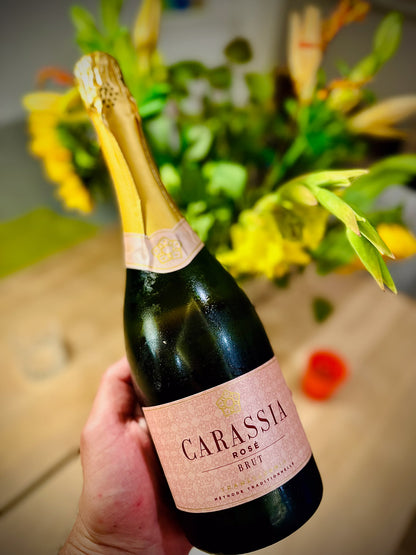 Bottle of Carassia Rose Brut sparkling wine held by a hand with flowers in the background
