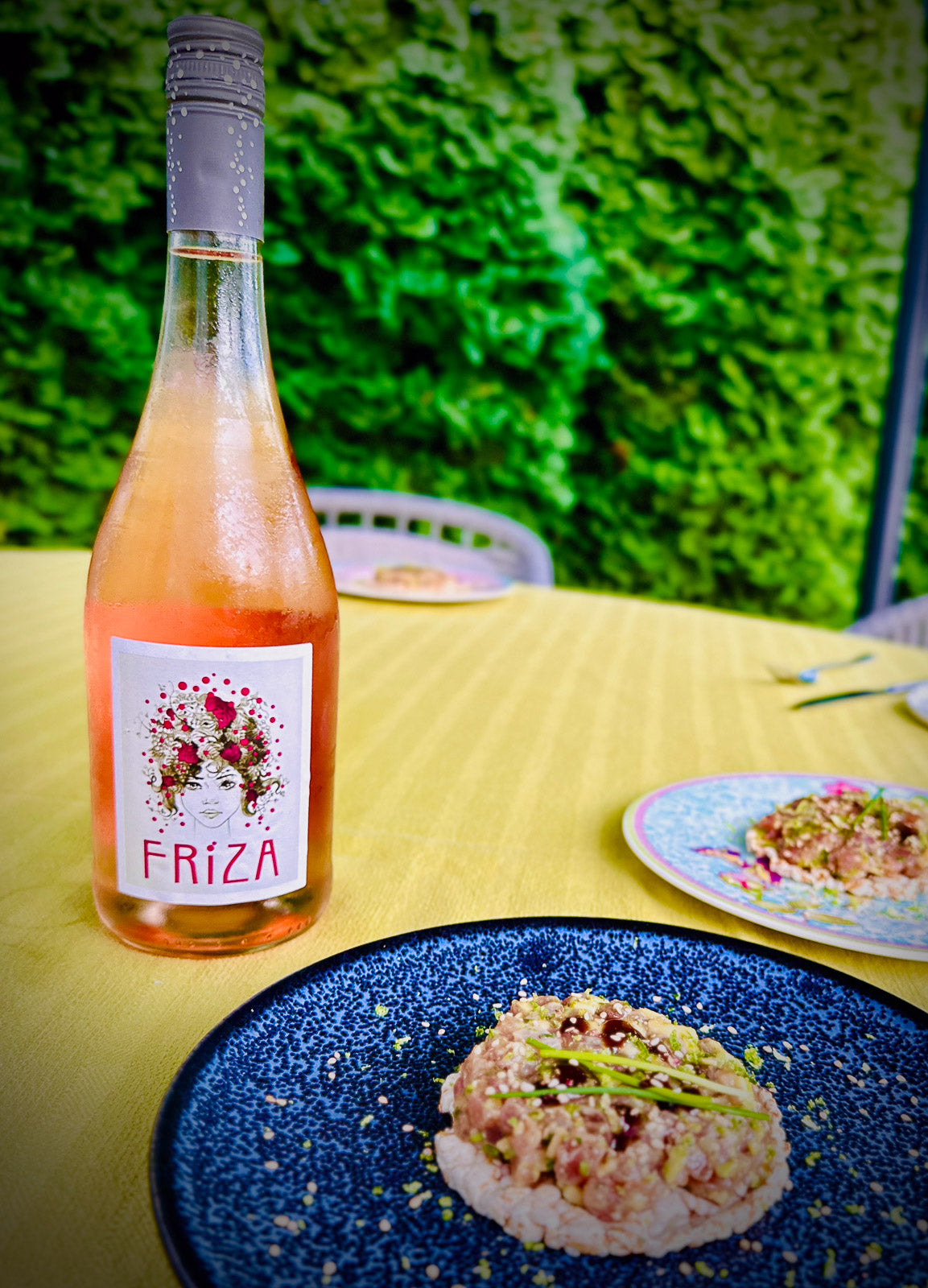 Bottle of Friza rosé wine on a table with food and greenery in the background