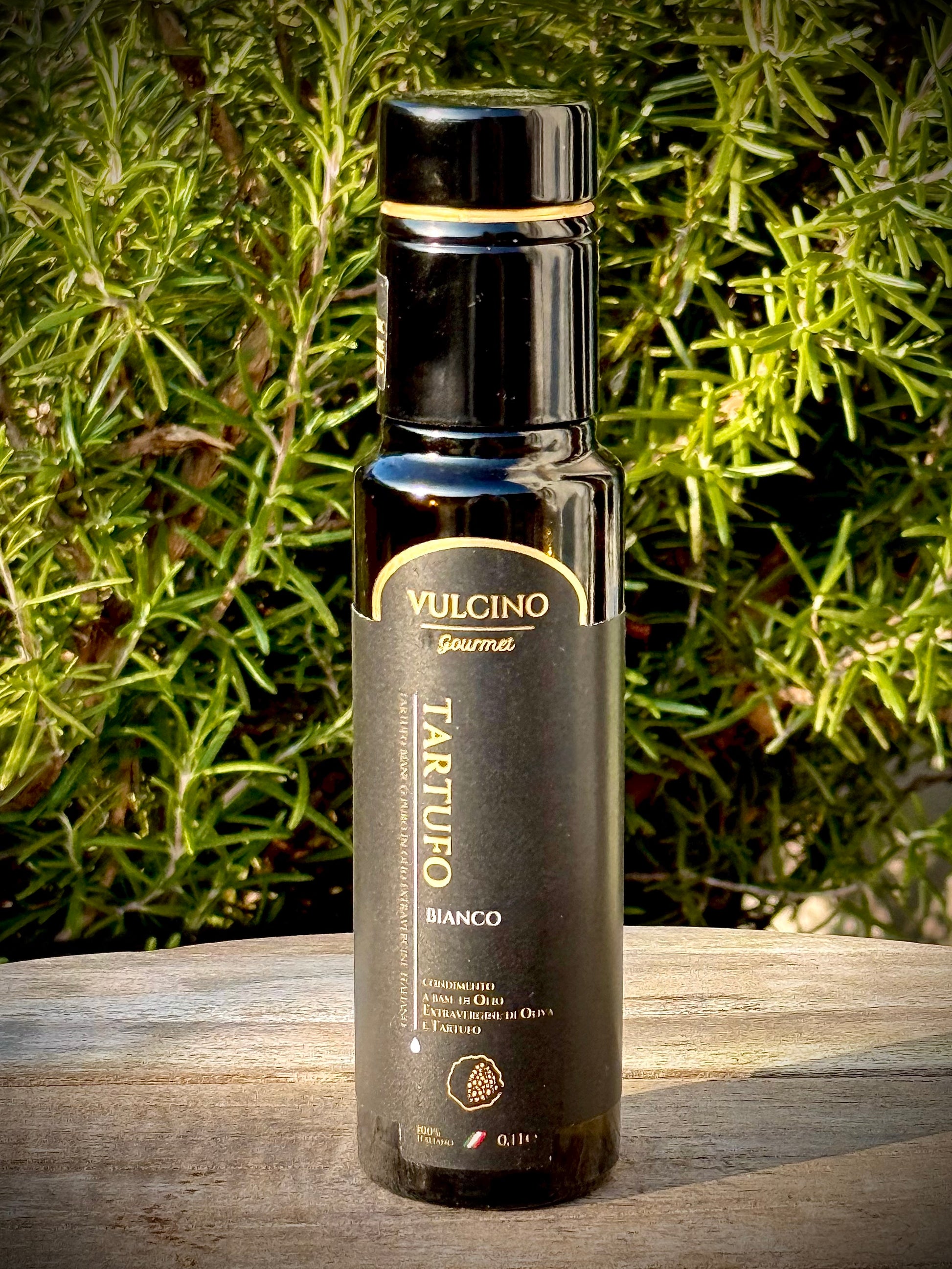 Vulcino Tartufo Bianco bottle on a wooden surface with greenery in the background