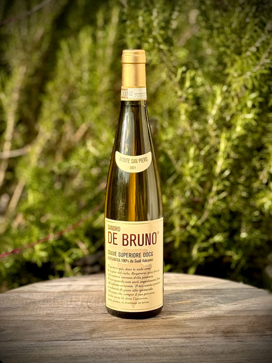 Wine bottle Soave Monte San Piero from Sandro De Bruno with a label on a wooden surface with a blurred green background