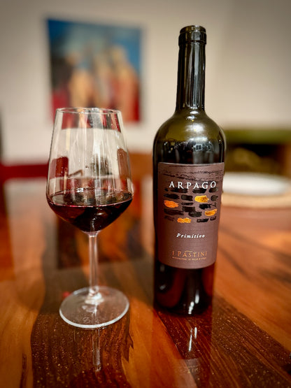 Bottle of Arpago wine with a glass of red wine on a wooden table.