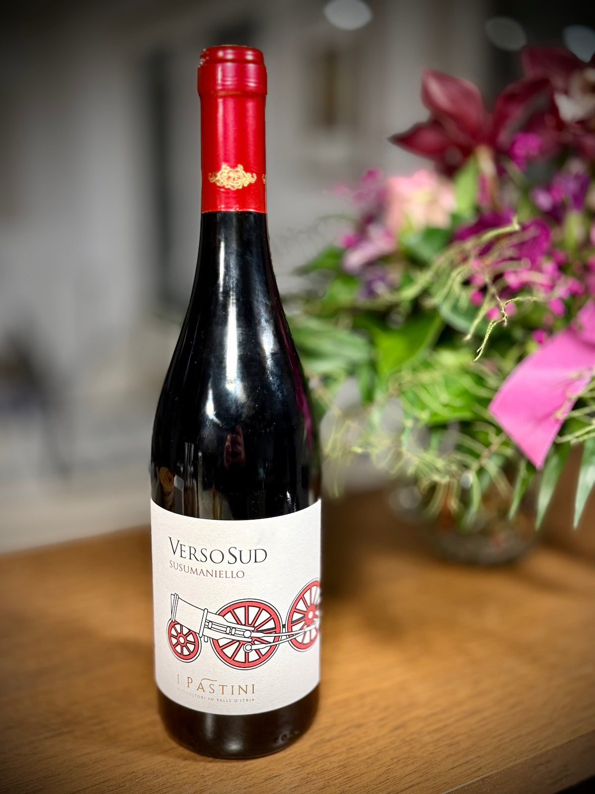 Wine bottle of Susumaniello named Versosud with red label on a wooden surface with flowers in the background