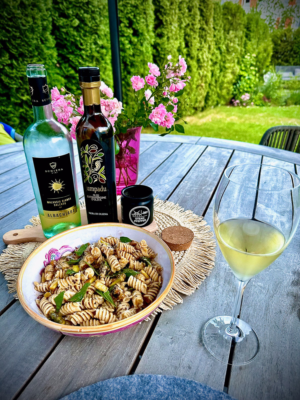 Pasta dish with wine bottles and a glass on a wooden table outdoors.