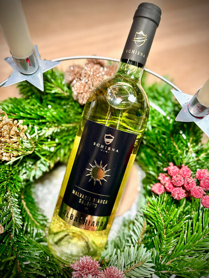 Bottle of white Malvasia wine with a decorative wreath and candles in the background