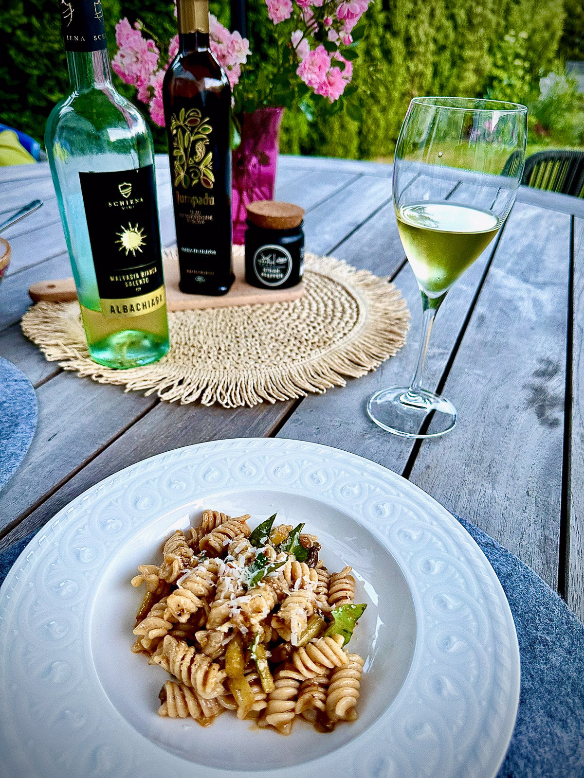Pasta dish with a glass of white wine on a wooden table outdoors.