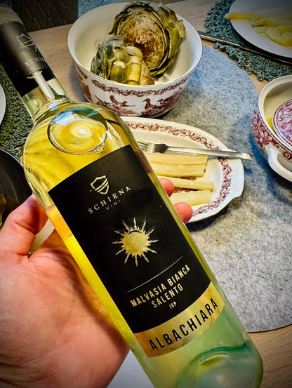 Bottle of Albachiara wine held by a hand with a table and food in the background