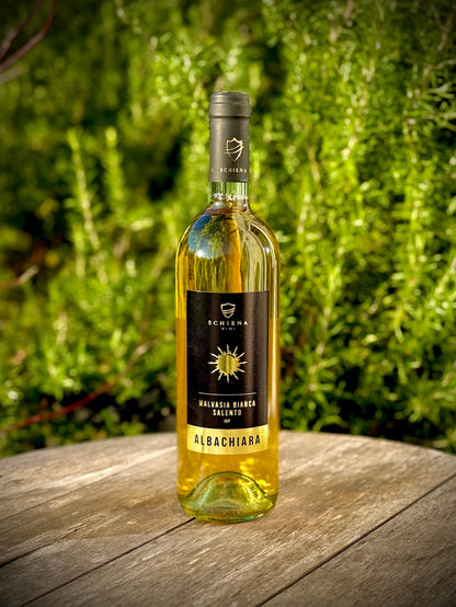 Bottle of Albachiara, a white malvasia bianca wine on a wooden surface with a green blurred background