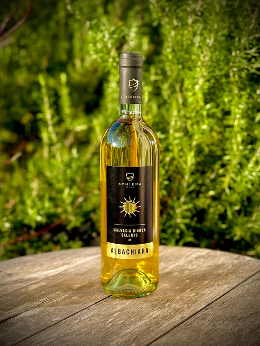 Bottle of Albachiara, a white malvasia bianca wine on a wooden surface with a green blurred background
