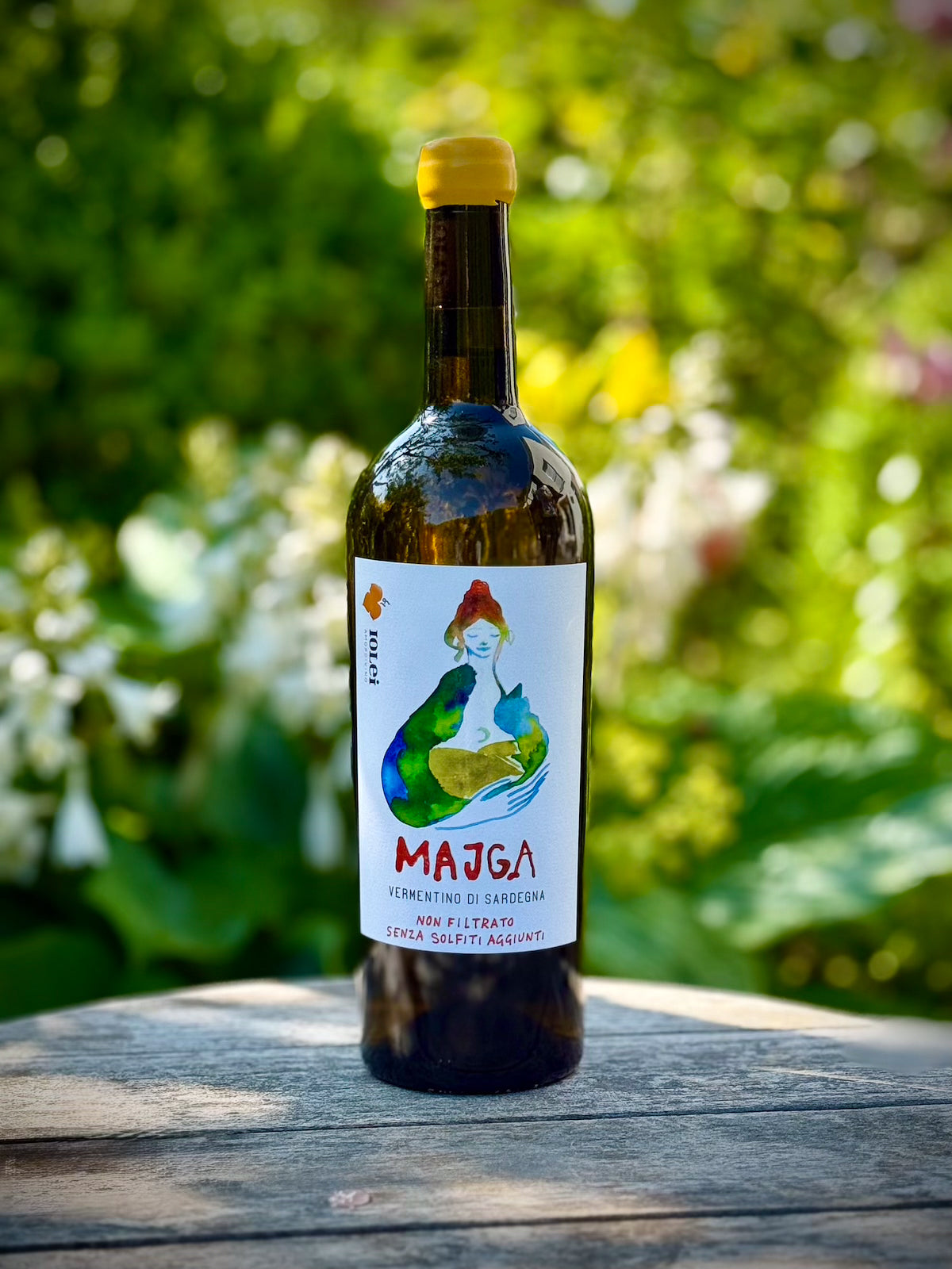 Bottle of Majga wine with a colorful label on a wooden surface with a blurred natural background