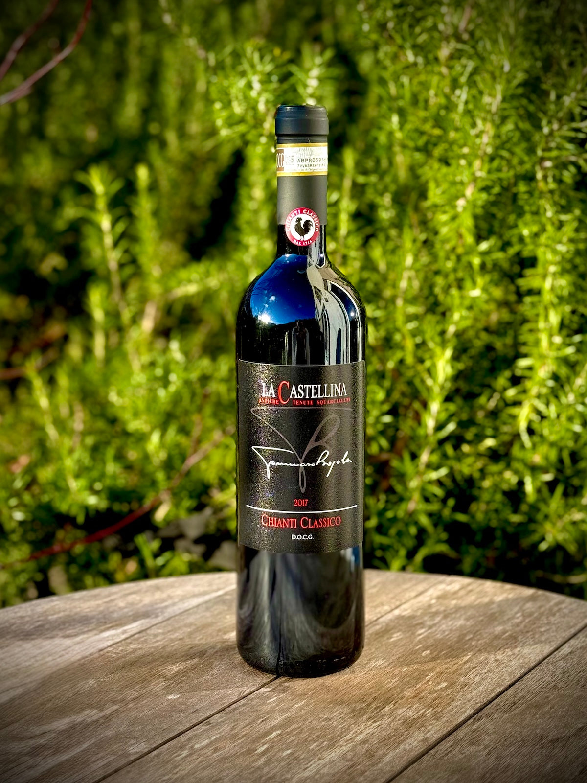 Chianti wine bottle 'La Castellina' on a wooden surface with greenery in the background
