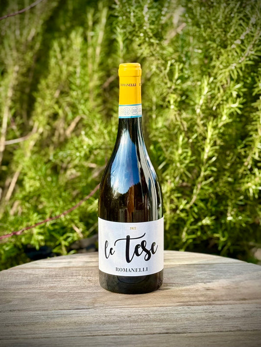 Wine bottle labeled 'le tese' from Romanelli on a wooden surface with a green, natural background