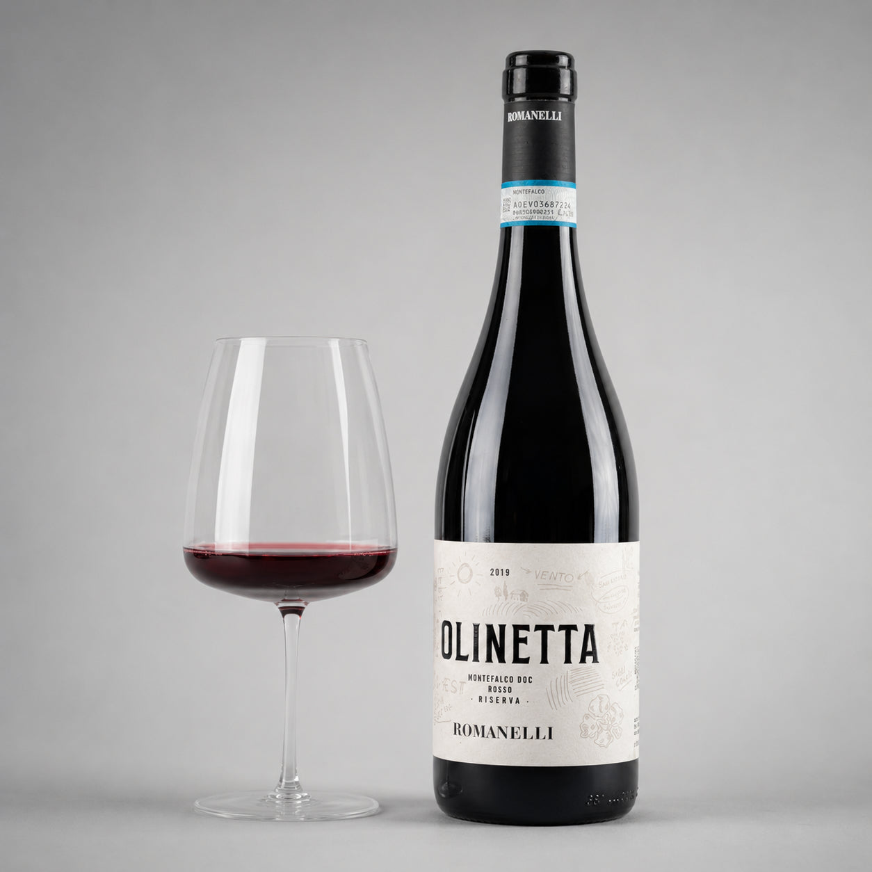 A glas of wine and the wine bottle Molinetta of type Montefalco from the producer Romanelli with label on a gray background