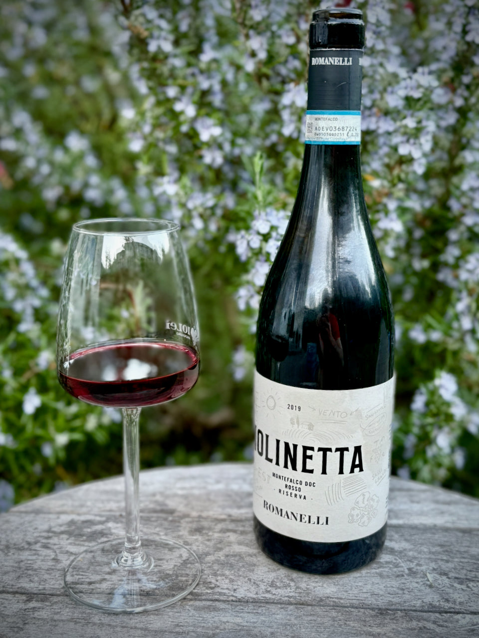 Eine Flasche Molinetta von Romanelli vor einem grünen Gartenhintergrund und Wein im Glas
