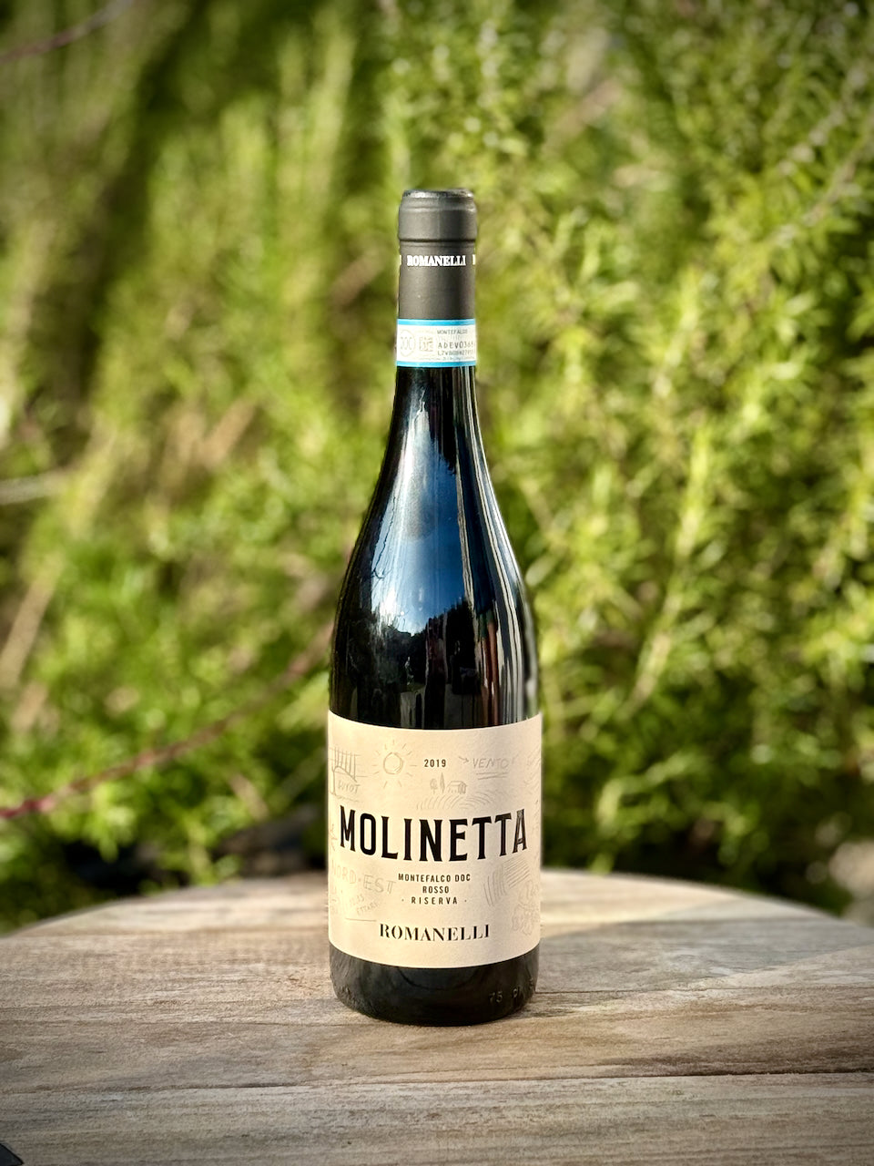 Eine Flasche Molinetta von Romanelli vor einem grünen Gartenhintergrund.
