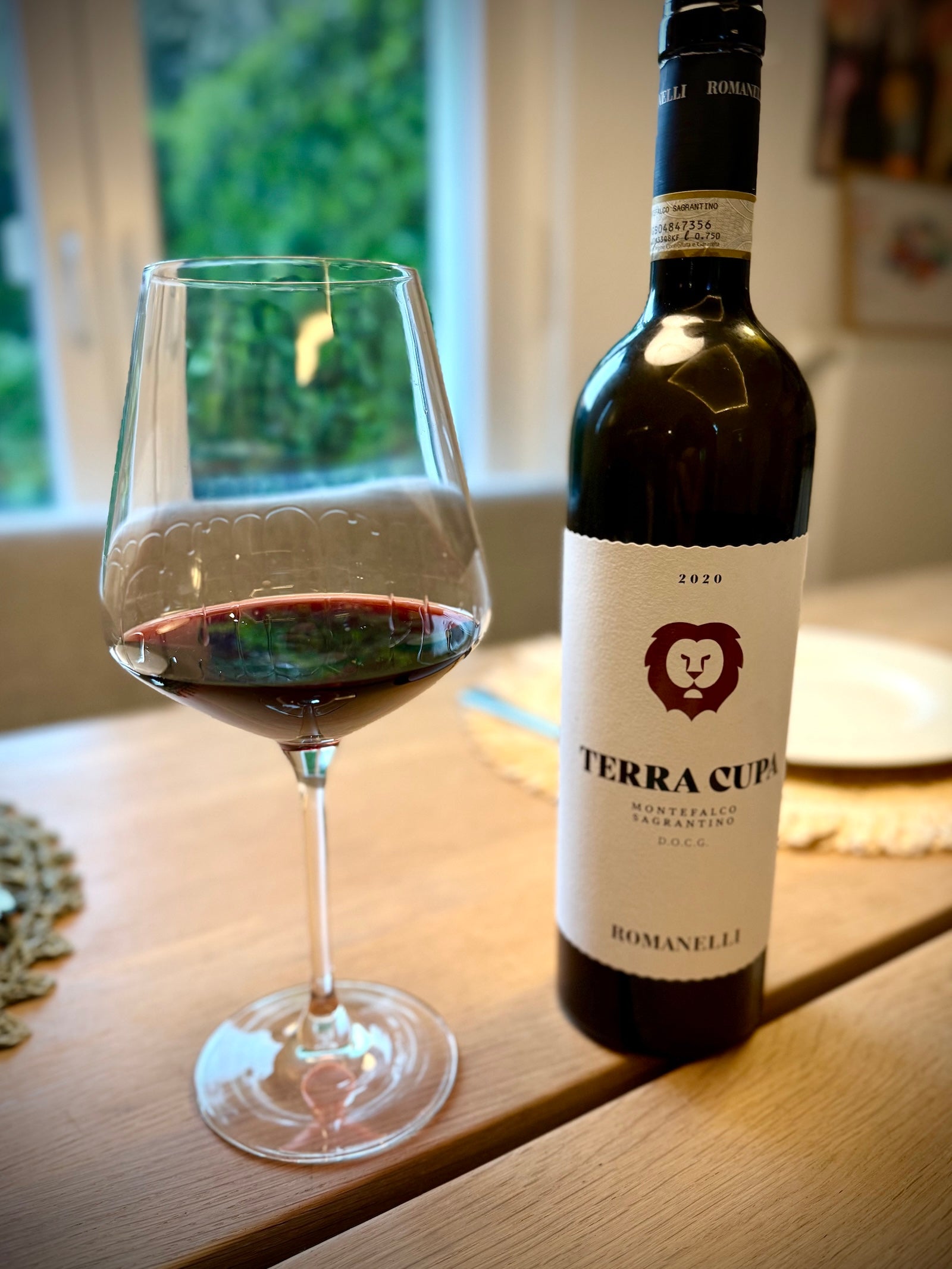 Bottle of Terra Cupa Romanelli wine with a glass of red wine on a wooden surface.