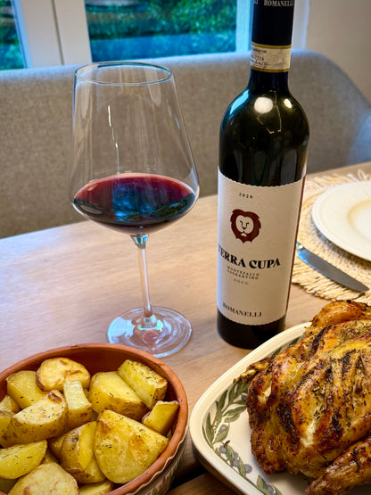 Bottle of Terra Cupa red wine with a glass, roasted potatoes, and roasted chicken on a table.