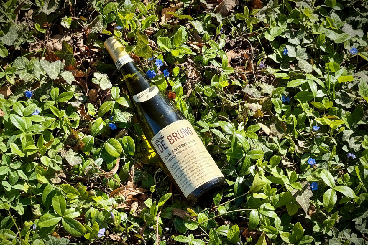 A Soave wine bottle from Sandro De Bruno  lying on green grass with small blue flowers.